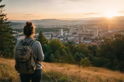 Person mit Rucksack steht bei Sonnenaufgang auf einem Hügel und blickt auf Stadt und Natur