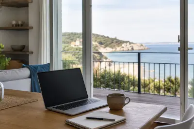 Laptop und Notizbuch auf einem Tisch in einer hellen Ferienwohnung mit Blick auf eine Küstenlandschaft